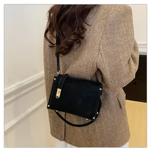 Détail du sac bandoulière en daim noir avec rivets dorés et fermoir sur blazer en tweed