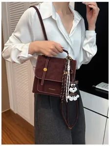 Dettaglio dello zaino in pelle bordeaux con cuciture a contrasto e ciondolo cane