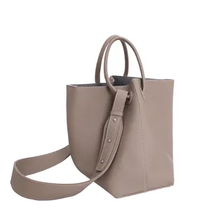 Minimalist taupe lychee leather bucket bag with wide shoulder strap and round handle