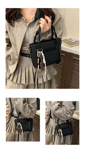 Detail of black leather tote bag with a chocolate charm and woven rope handle accents