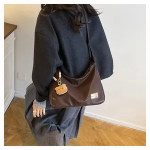 Detail of matte brown leather tote bag featuring a plush bear charm and fashion patch
