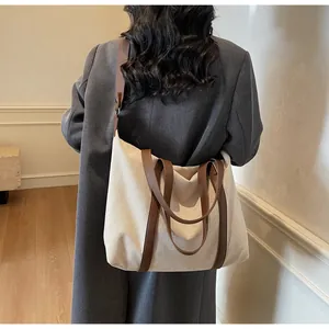 Close-up of a large canvas tote bag with brown leather handles shown on shoulder