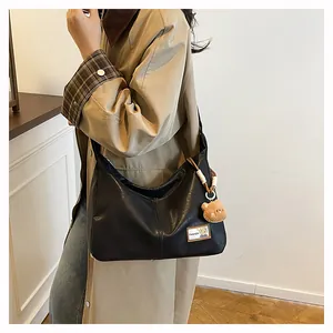 Detail of black PU leather half-moon bag with fashion patch and plush bear charm