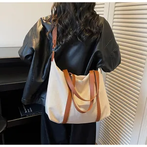 Detail view of cream canvas tote bag with brown leather straps worn by model
