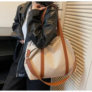 Detail of canvas tote bag with brown leather handles on a model in black leather jacket