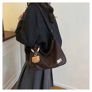 Detail of dark brown tote bag showing the fashion label and a plush bear pendant charm