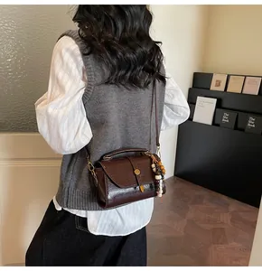 Detail view of brown patent leather bag with round metal buckle and wood bead charm