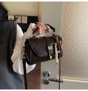 Detail of dark brown leather Boston bag with vintage texture and wooden bead charm
