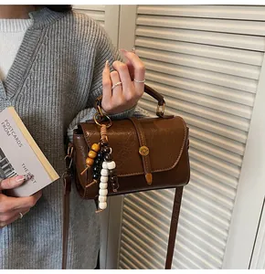 Close-up of vintage brown leather Boston bag with metal lock and colorful bead charm