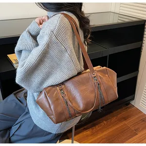Brown Boston bag with heart pendant and decorative zippers shown from a side view