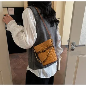 Detail of yellow quilted suede bucket bag with gold chain and metal twist lock
