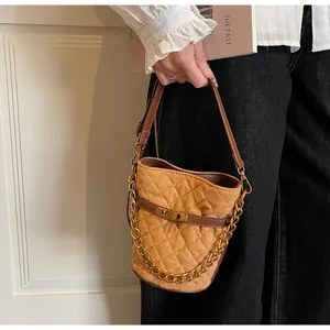 Close-up of brown quilted suede bucket bag with gold chain and metal twist lock