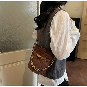 Detail of brown quilted crossbody bag with gold chain and buckle on female model