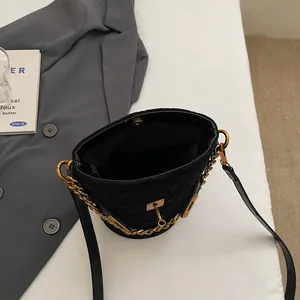 Minimalist black quilted bucket bag with gold chain strap on a professional backdrop