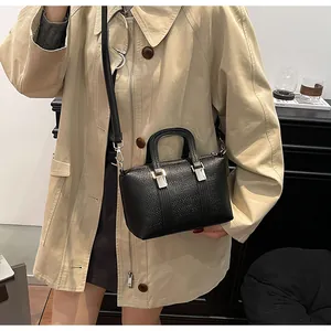 Detail of black textured Boston bag with silver buckles styled on a khaki trench coat