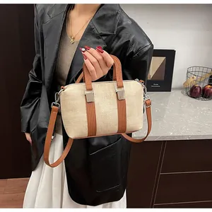 Detail of a straw Boston bag with brown leather handles worn by a model in a suit