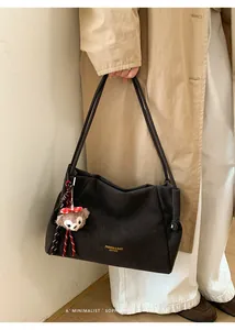 Détail du cabas en cuir mat foncé avec logo doré et pendentif ours en peluche