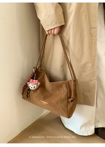 Détail d'un sac cabas en daim marron avec charm en peluche et lettrage doré chic