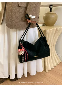 Détail du sac hobo en daim noir avec texte doré et breloque ours en style urbain