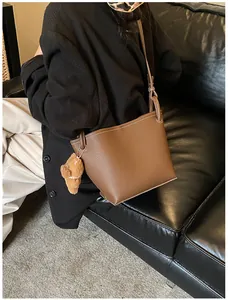 Détail du sac seau marron à motif litchi avec surpiqûres blanches et charme d'ours