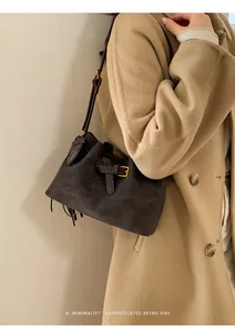 Détail du sac seau rétro en daim avec boucle dorée et pompon sur manteau en laine