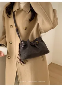 Détail du sac seau en daim marron foncé avec sangle en cuir et pompon cœur sur un manteau