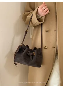 Détail du sac seau rétro en daim avec boucle et pompon sur un manteau camel