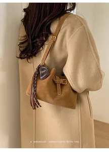 Détail du sac seau en daim marron avec gland en cuir et pendentif B sur un manteau beige