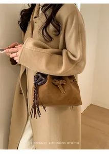 Détail du sac seau en daim marron avec des pompons à franges et une sangle à boucle