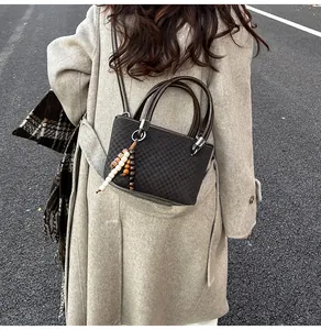 Detail of dark brown checkered bucket bag with wooden bead charm and long shoulder strap