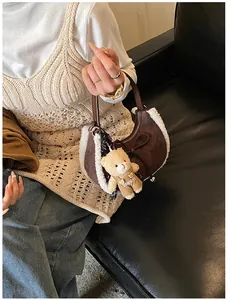 Close-up of brown suede crescent bag with faux fur trim and cute teddy bear charm