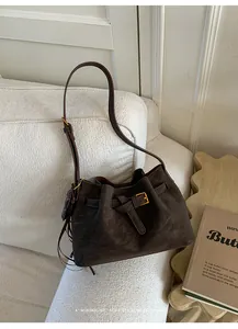 Détail du sac seau en daim marron foncé avec bandoulière réglable sur un canapé