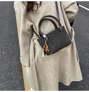Detail view of checkered bucket bag with beaded charm and leather strap on winter coat