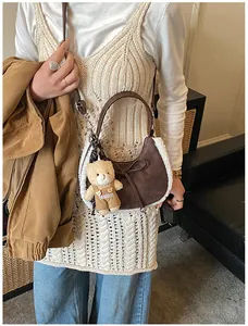 Detail of brown suede crescent bag with plush shearling trim and cute teddy bear charm