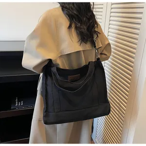 Detail of black canvas tote bag worn with a beige trench coat for a stylish office look
