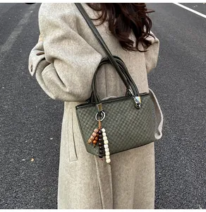 Detail of dark green bucket bag with grid texture and colorful ethnic bead charm