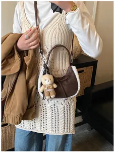 Detail of brown suede crescent bag featuring plush white trim and a cute bear charm