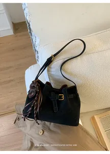 Détail d'un sac seau en daim noir avec boucles dorées et pompon en cuir sur un canapé