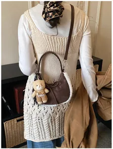 Detail of suede crescent bag with plush trim and cute bear charm shown on a shoulder