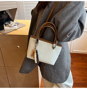Detail of a minimalist beige bucket bag with brown leather handles and a beaded charm
