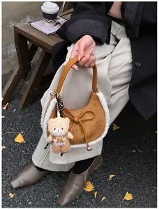 Close-up of brown suede crescent bag with white faux fur trim and cute teddy bear charm