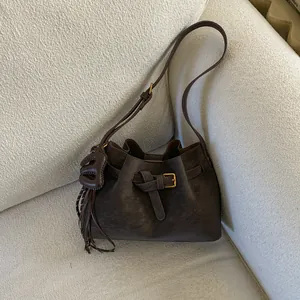 Sac seau rétro en daim marron foncé avec sangle en cuir et pompon sur canapé