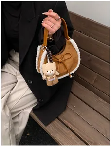 Detailed shot of brown suede crescent bag featuring plush sheepskin trim and a teddy charm
