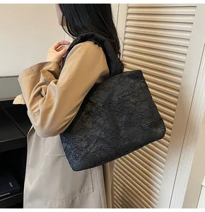 Detail of black embossed tote bag with 3D texture shown on model in warm lighting