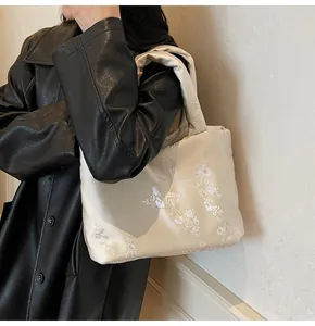 Detail of floral embroidery on ivory satin jacquard tote bag held by model
