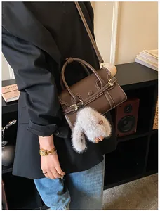 Detail view of dark brown structured crossbody bag with white stitching and plush rabbit charm