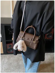 Detail of dark brown handbag with white stitching and grey plush bunny charm