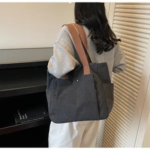 Detail of black canvas tote bag with wide brown straps and side pockets on a model