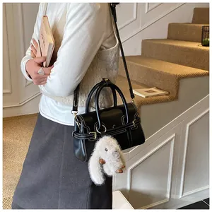 Detail of a black leather crossbody bag with white contrast stitching and a plush rabbit charm