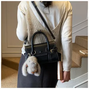 Detail of black crossbody bag with contrast stitching and plush rabbit charm on stairs